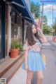 A woman in a blue skirt is standing on the sidewalk.