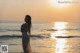 A woman in a white dress standing in the ocean at sunset.