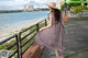 A woman in a dress and hat walking along the beach.