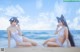 Two women in white bathing suits sitting on the beach.