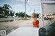 A woman in a red top standing next to a white car.