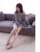 A woman sitting on a couch wearing a gray sweater dress.