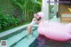 A woman in a white bathing suit standing next to a pink flamingo.